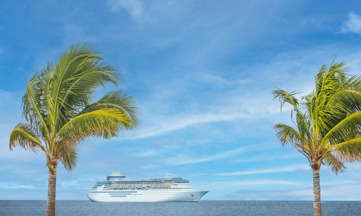 Kreuzfahrtschiff auf blauem Meer, umrahmt von zwei Palmen vor einem leicht bewölkten Himmel. Kreuzfahrtschiff auf blauem Meer, umrahmt von zwei Palmen vor einem leicht bewölkten Himmel.